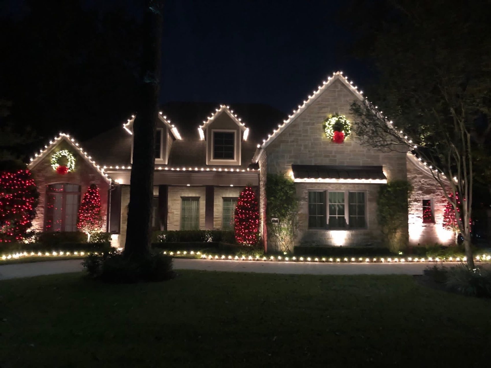 Stone home with wreaths and rooflines outlined in Christmas lights